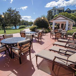 A sunny outdoor patio area featuring tables, chairs, and lounge chairs with a gazebo in the background.