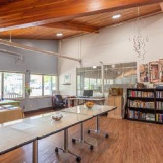 A modern open-plan office with a wooden ceiling, featuring desks, chairs, and a bookshelf.