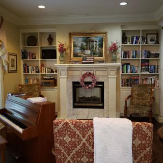 A cozy living room featuring a fireplace, bookshelves filled with books, and a piano.