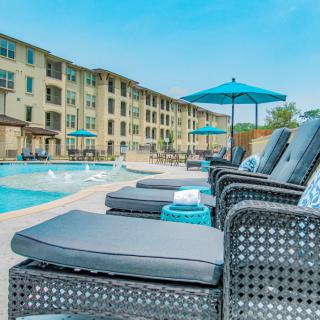 Outdoor pool area with sun loungers and umbrellas at an apartment complex.