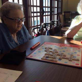 Two elderly individuals playing Scrabble by a window.