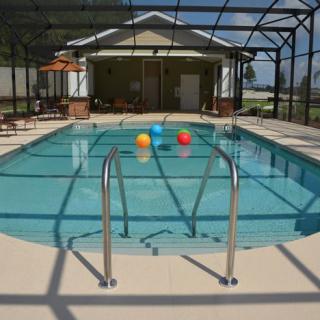 A sunny indoor swimming pool with colorful balls floating and a ladder at the entry.