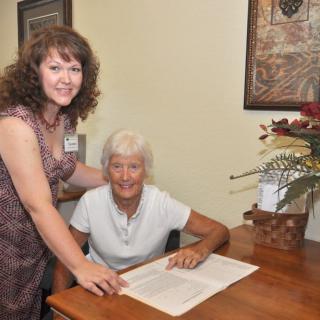 Two people smiling while sitting at a table with documents and decorative items.