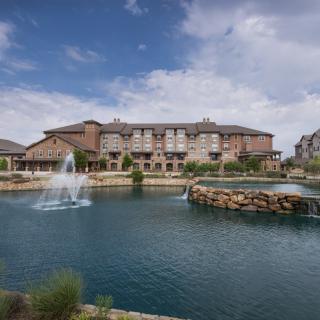 A picturesque hotel resort with a lake and water fountain under a blue sky.