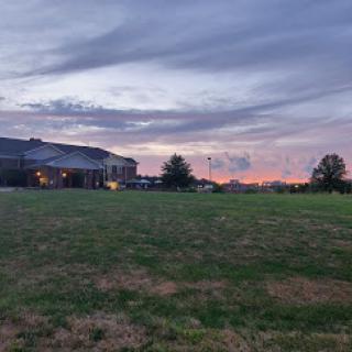 A beautiful sunset casts warm hues over a grassy field with a distant building.