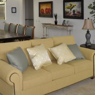 A cozy living room with a yellow sofa and decorative pillows, flanked by a lamp and artwork on the walls.