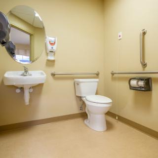 A clean and accessible restroom featuring a toilet, sink, and safety handrails.