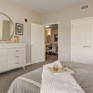 A neatly arranged bedroom with neutral tones, featuring a large mirror and a white dresser.