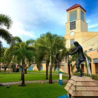 A scenic view of a park featuring a statue, lush palm trees, and a building with a clock tower.