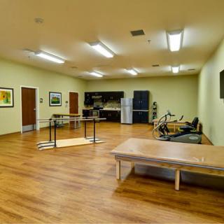 A rehabilitation room equipped with exercise machines and therapy tables on a wooden floor.