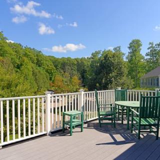 A sunny outdoor deck with green furniture overlooking a lush, tree-filled landscape.