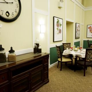 A cozy dining area with a wall-mounted clock, artwork, and a neatly set table.