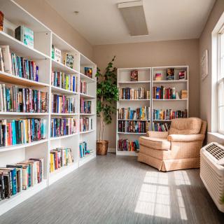 A cozy reading corner in a library with bookshelves filled with books and an armchair by the window.