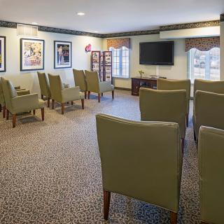A well-lit meeting room with multiple chairs arranged in rows facing a television, decorated with framed art on the walls.