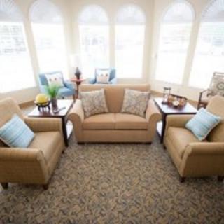 A cozy living room with a central sofa, armchairs, and a coffee table surrounded by large windows.