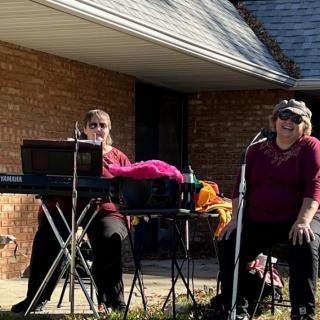 Two musicians perform outdoors with a keyboard and microphone setup.