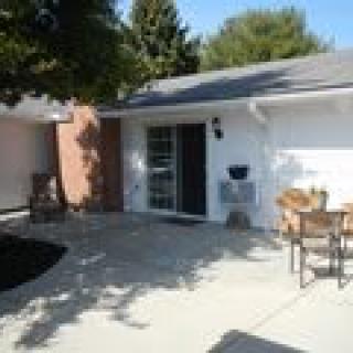 A cozy patio area outside a house with outdoor furniture and a tree providing shade.