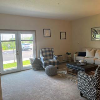 A cozy living room with a sofa, armchairs, and a coffee table, well-lit by natural light through the windows.
