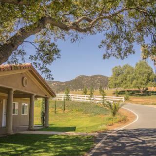 A picturesque countryside scene with a house, winding road, and lush greenery under a clear blue sky.