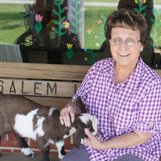 A cheerful woman interacts with a playful goat outdoors.