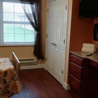 A cozy room with a bed, window, and dresser topped with a TV.