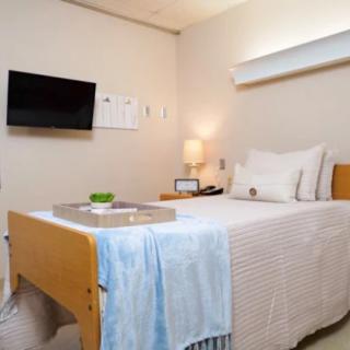 A clean and tidy hospital room with a bed, television, and lamp.