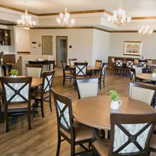 A well-lit dining area with multiple tables and chairs, featuring elegant chandeliers and wooden flooring.