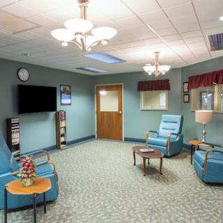 A cozy waiting room with blue chairs, a television, and decorative lighting.