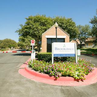 Entrance to a residential complex with a sign and landscaped surroundings.
