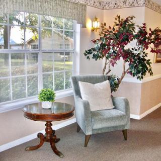 A cozy corner featuring a green armchair, a small wooden table, and a decorative plant by the window.