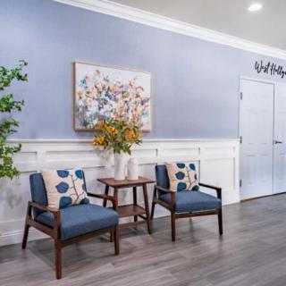 A cozy waiting area with two chairs, a small table with a flower vase, and wall art.