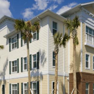 A modern residential apartment building with palm trees under a sunny sky.
