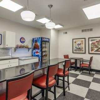A comfortable break room featuring red chairs, a long table, a vending machine, and checkered flooring.