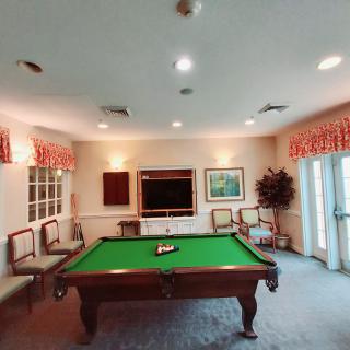 A cozy game room featuring a pool table with green felt, surrounded by decorative chairs and a warm interior.