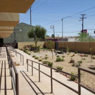 A pathway with handrails leading through a desert landscaped area beside buildings on a sunny day.