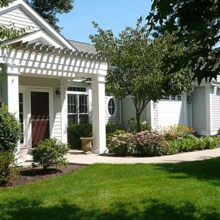 A charming house with a well-maintained garden and lush green lawn under a clear blue sky.