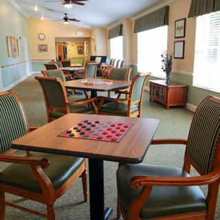 A community room with a checkerboard on the table, surrounded by comfortable seating and large windows.