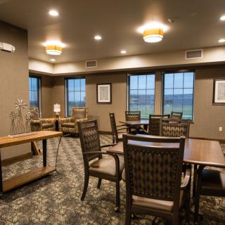A cozy dining area with multiple tables and chairs, featuring large windows and warm lighting.