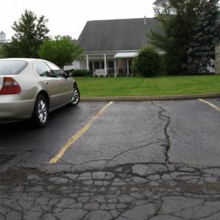 A silver car parked in a lot with a grassy area and a house in the background.
