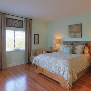 A cozy bedroom with a wooden floor, featuring a neatly made bed and a window with curtains.