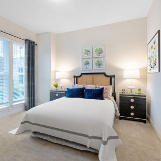 A modern and cozy bedroom featuring a double bed with navy blue pillows, flanked by two nightstands with lamps, and decorated with wall art.