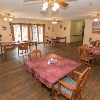 A dining area with neatly arranged tables and chairs, featuring wooden floors and ceiling fans.