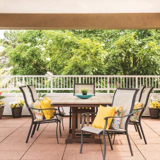 An inviting patio setup with a wooden table, chairs adorned with yellow cushions, and a lush garden view.