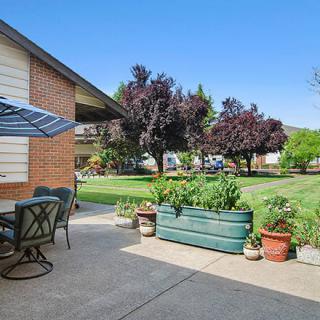A cozy patio area with a table, chairs, and umbrella surrounded by potted plants overlooking a landscaped garden.