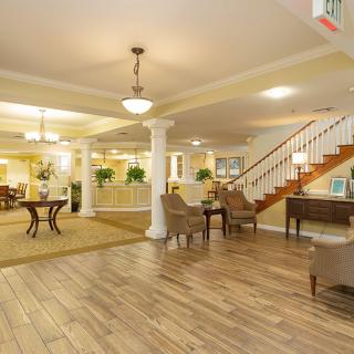 A spacious and elegantly designed lobby featuring hardwood floors, comfortable seating, decorative columns, and a staircase.