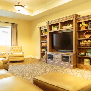 A cozy living room with a large TV, comfortable seating, and decorative shelves.