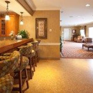 A cozy interior featuring a bar area with seating and warm lighting, leading into a lounge space.