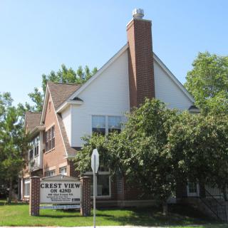 A brick church building with a prominent chimney, surrounded by trees and a sign in front.