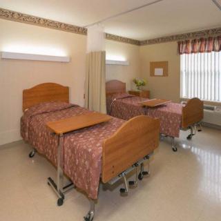 A clean and well-organized hospital room featuring two beds with wooden headboards and matching bedding.
