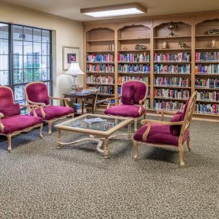 A cozy library reading room with bookshelves, plush seating, and a central table.